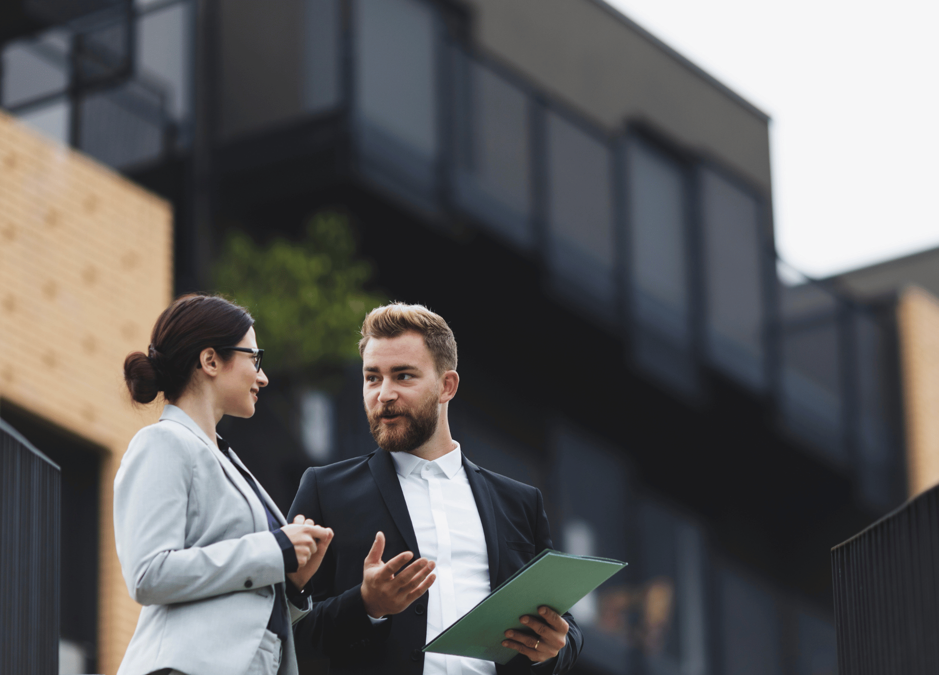 Two professionals discussing business outside a modern building, symbolizing real estate and property management.
